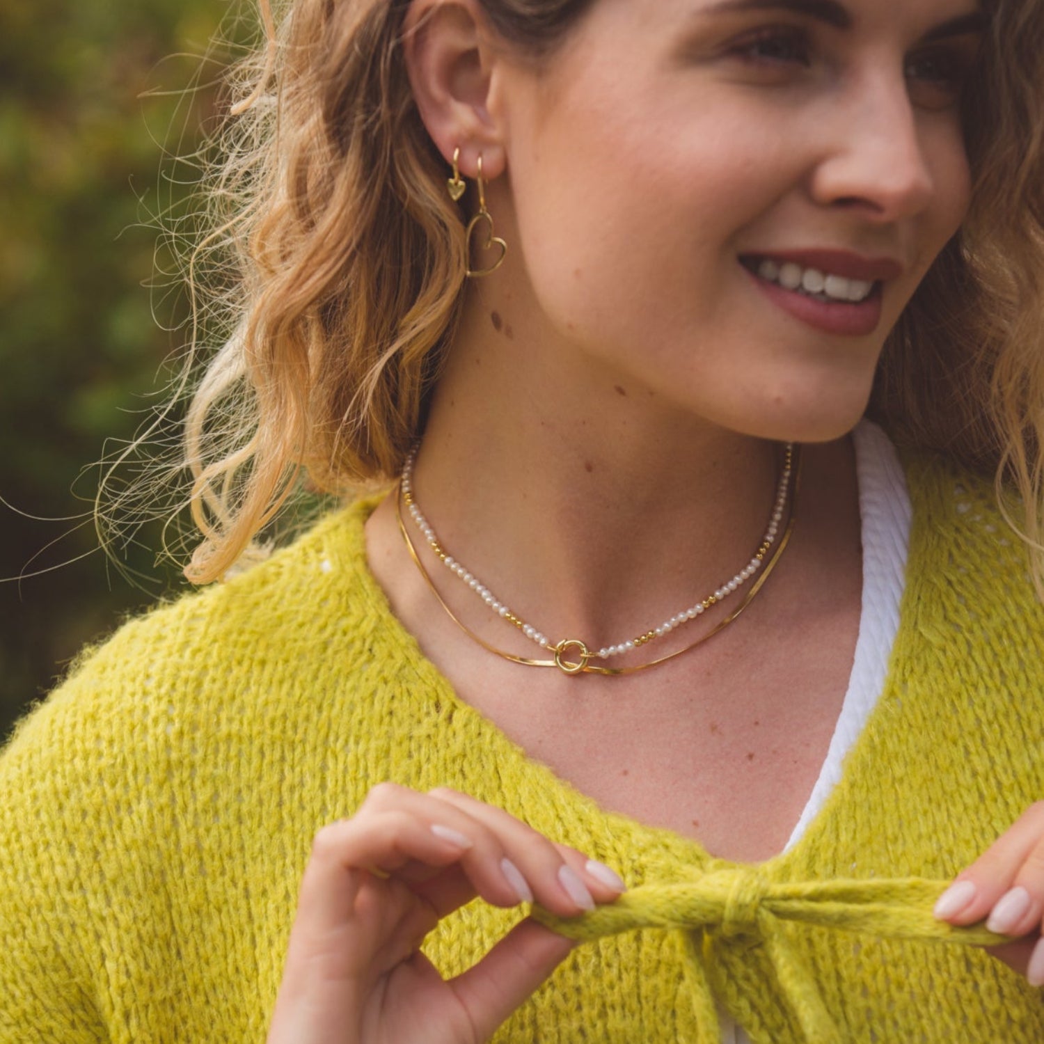 A fine gold plated snake chain, layered with a pearl bead necklace and shown being worn on a model.