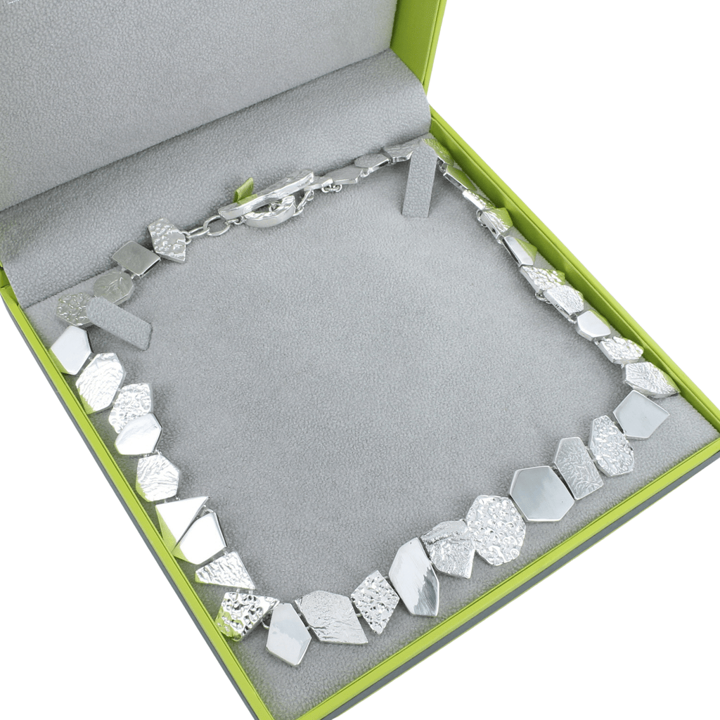 A sterling silver necklace comprising of geometric shapes with varying textured finishes, shown in a Reeves & Reeves grey and green gift box.