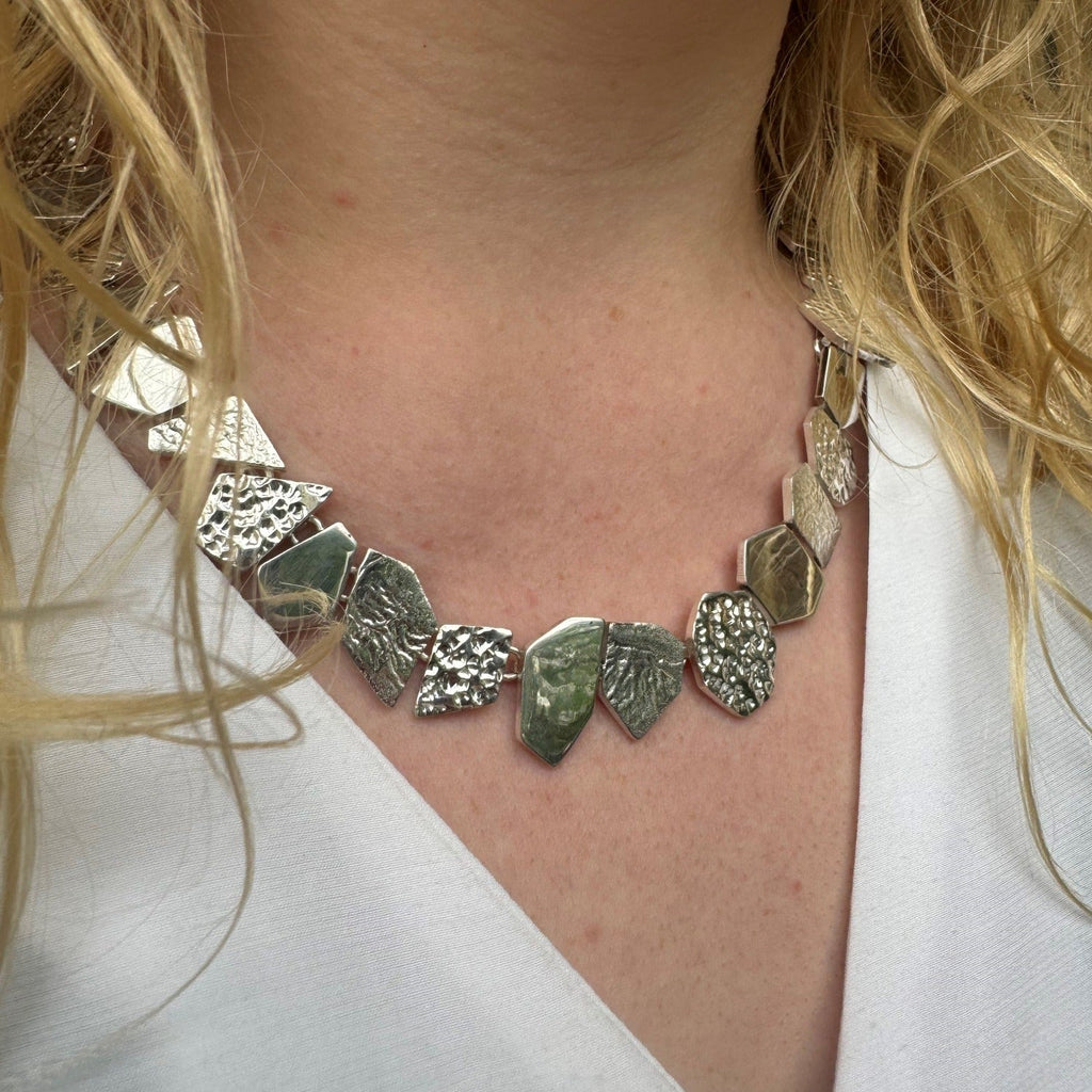 A sterling silver necklace comprised of geometric shapes with varying textured finishes, worn on a models neck.