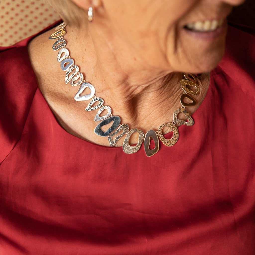 A sterling silver necklace with irregular shapes that have varying textures, worn on a ladies neck.