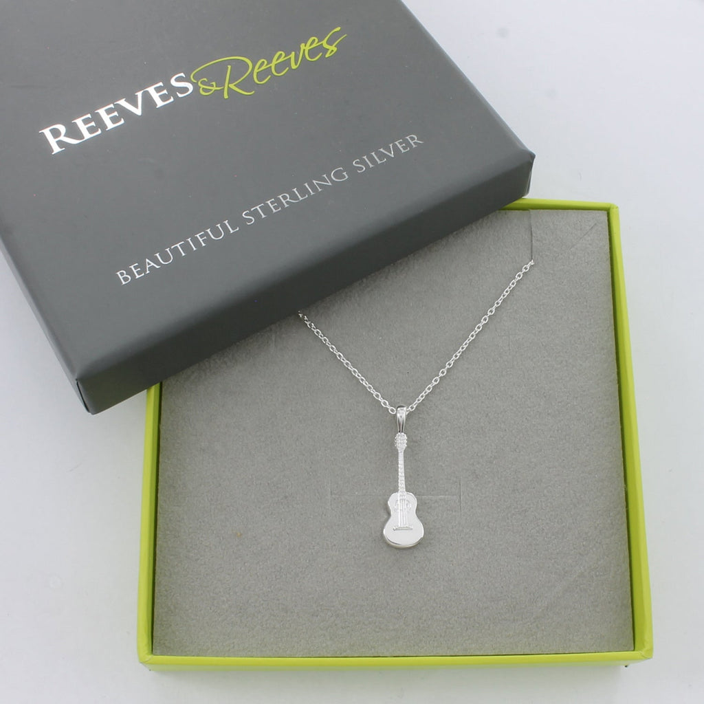 A Sterling Silver guitar pendant, hanging on a silver chain and shown in a Reeves & Reeves grey and green branded gift box.