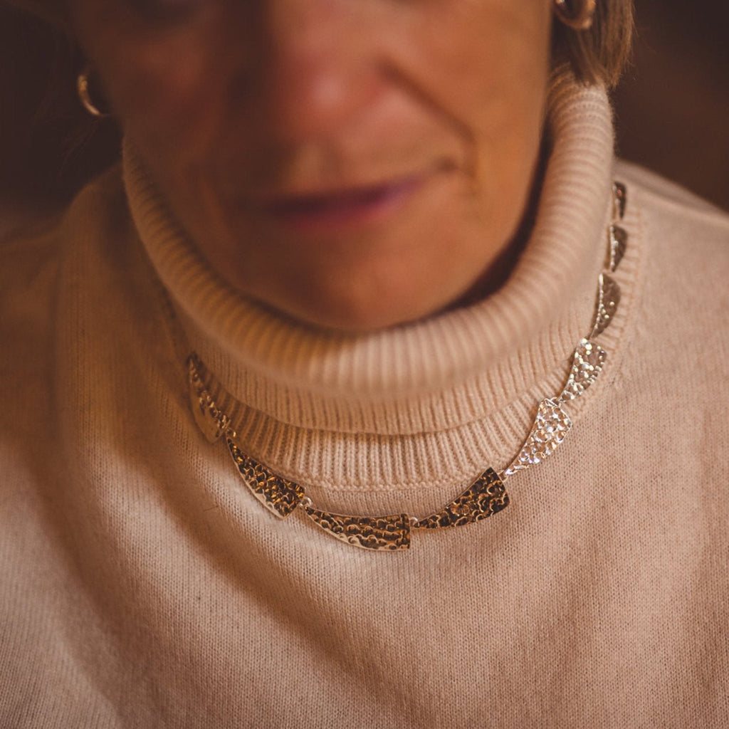 A sterling silver necklace made up of sail style shapes with a hammered finish, worn on a models neck.