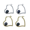 Two pairs of heart shaped hoop earrings, one silver and one gold plated, with dark peacock pearls sitting inside each heart.