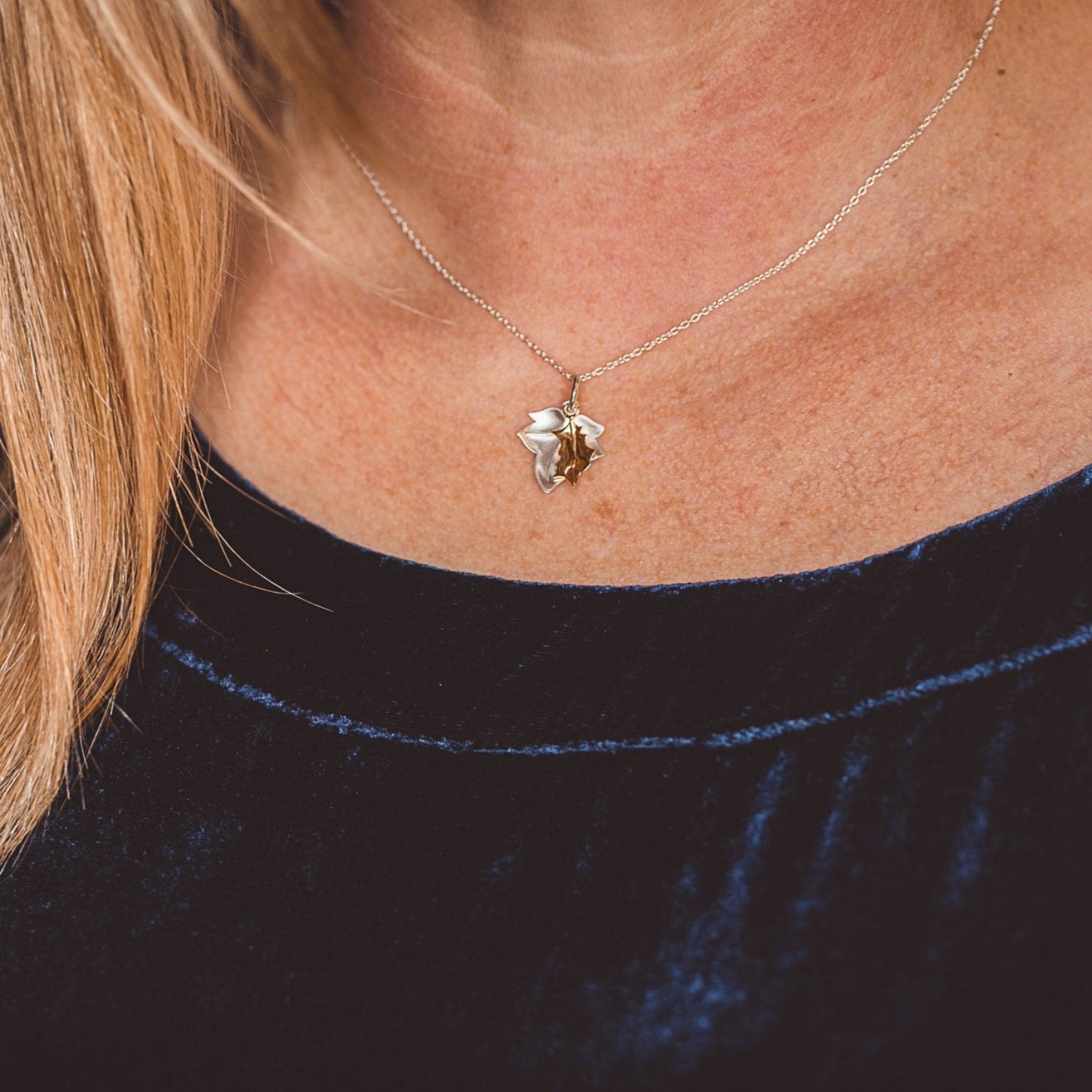 A sterling silver ivy leaf with a smaller gold plated holly leaf hanging on top and both hanging from a silver chain, worn on a models neck.