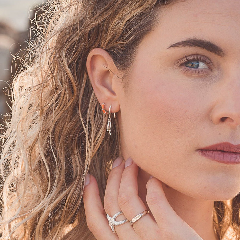 A sterling silver drop style earring with two little fish hanging from the bottom of a silver hook. Shown in a models ear.