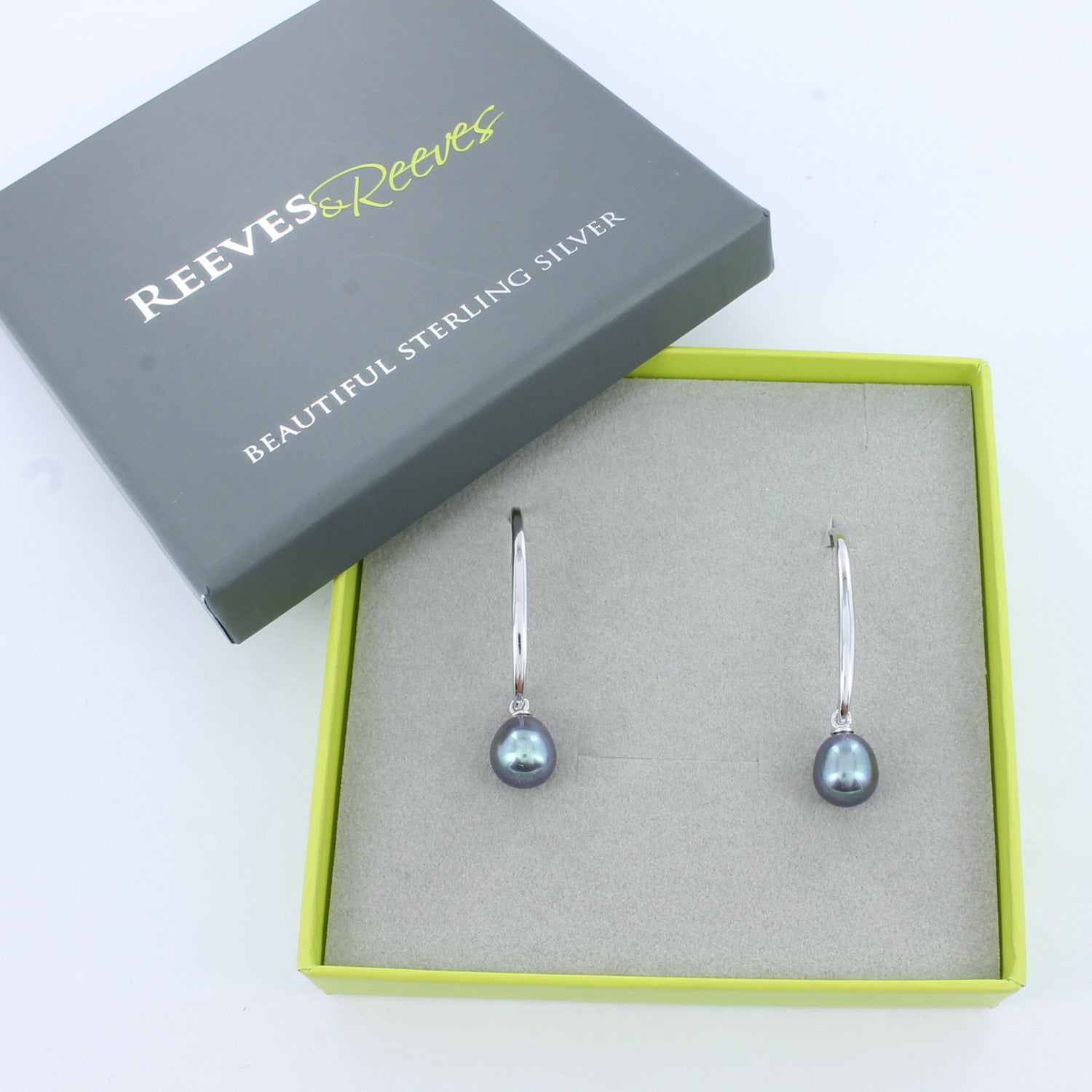 Sterling Silver long loop drop earrings with peacock colour pearls hanging from the bottom, shown in a Reeves gift box.