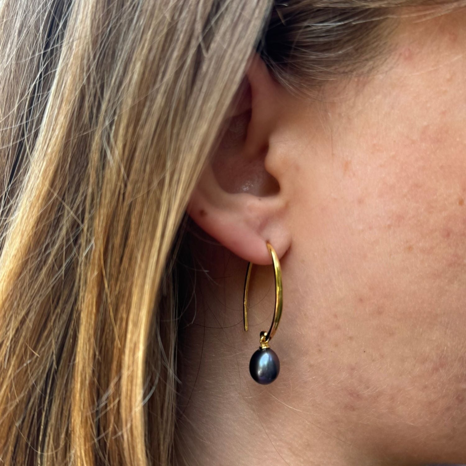 A pair of gold plated long loop hook earrings with a dark peacock colour freshwater pearl hanging from the bottom.