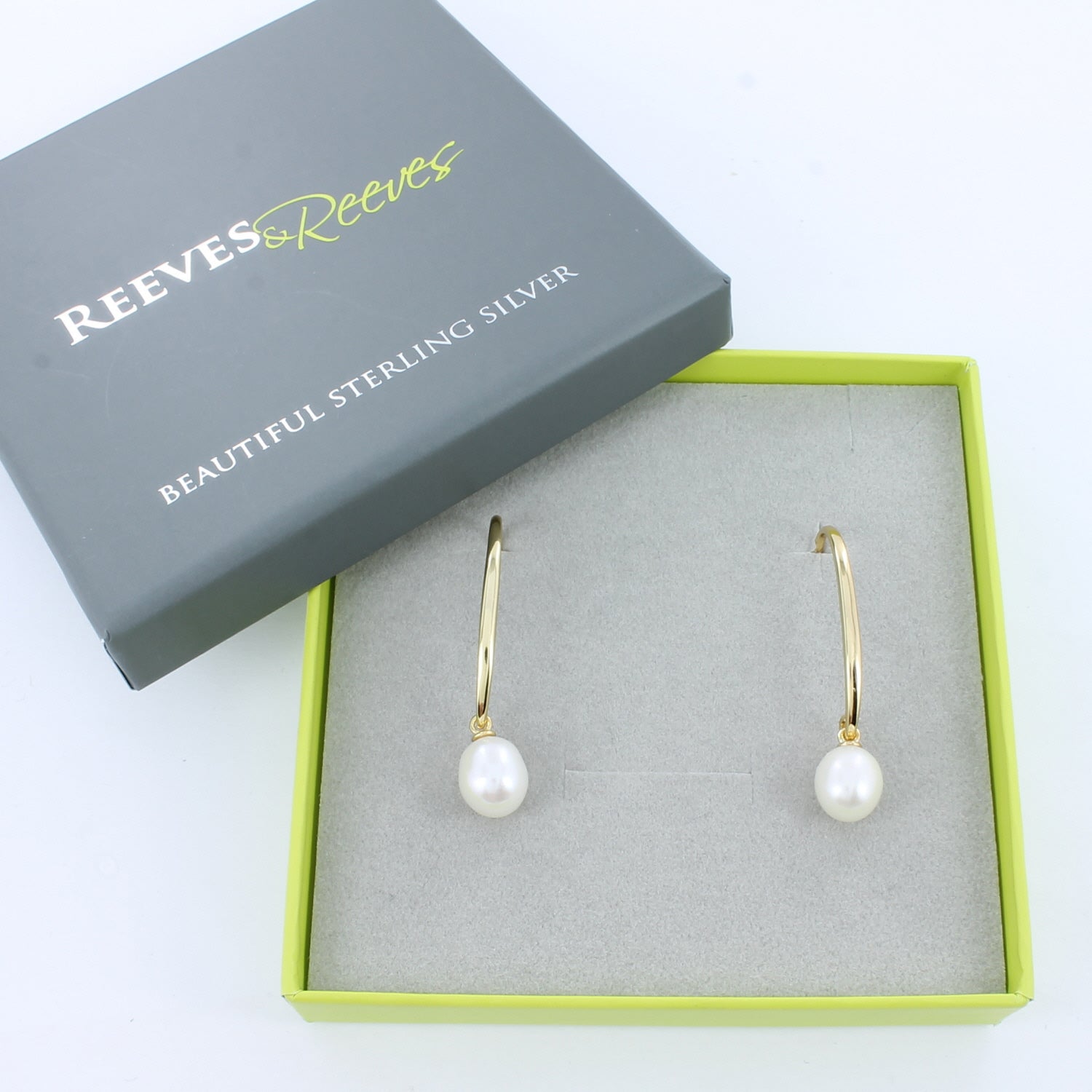 A pair of 18ct gold plated hook earrings with a white freshwater pearl hanging from the bottom. Shown in a Reeves & Reeves grey and green branded gift box.