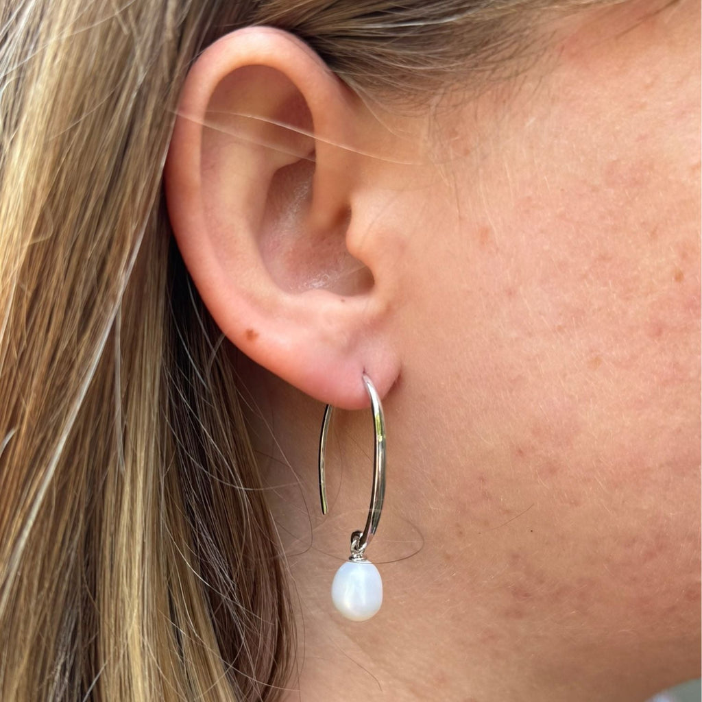 Sterling Silver hook style drop earring with a white freshwater pearl hanging from the bottom. Worn in a ladies ear.
