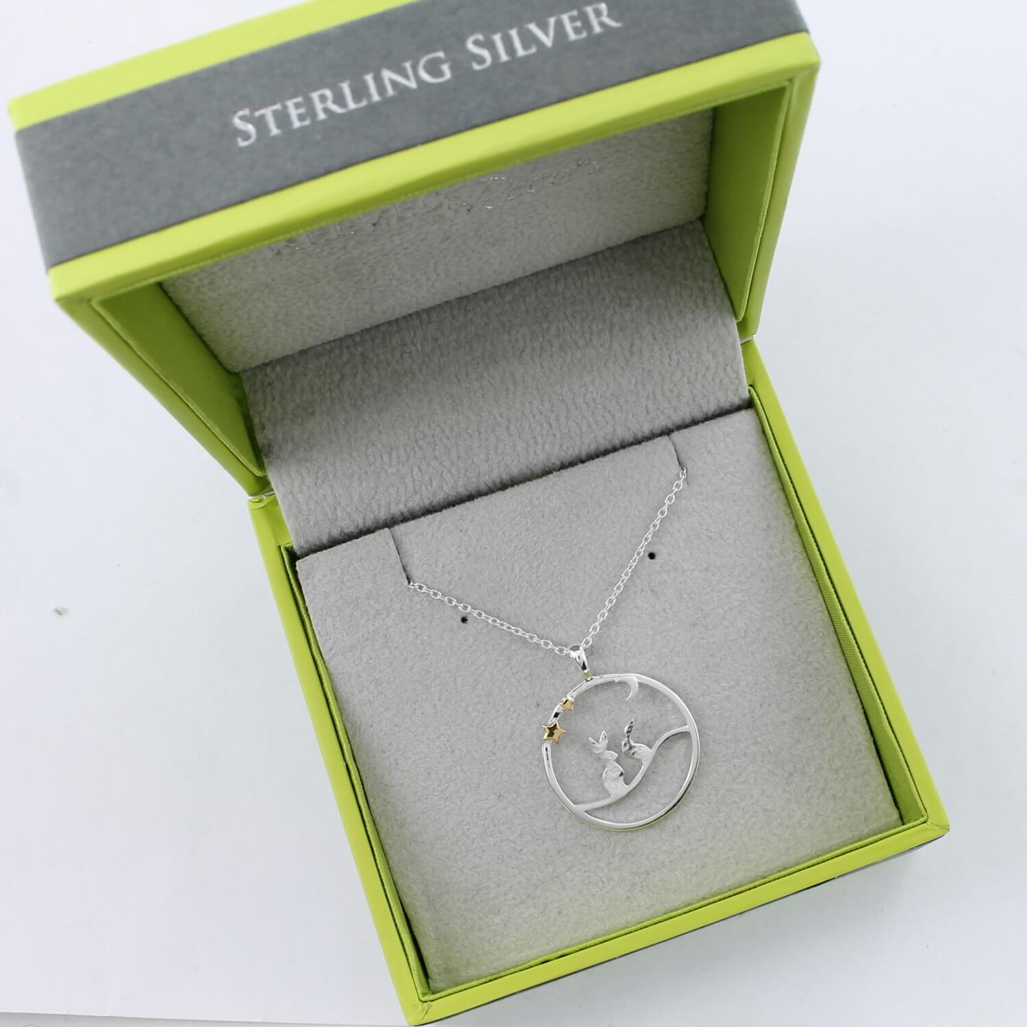 Two Silver Hares sat under a silver moon and two gold plate stars, hanging on an adjustable chain. The pendant is in a Reeves & Reeves branded gift box in green and grey colours.