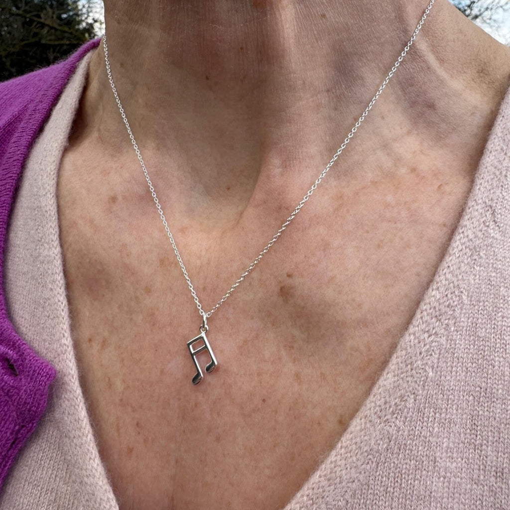 A Sterling Silver Music Note Necklace, hung on a silver adjustable chain and worn on a models neck.