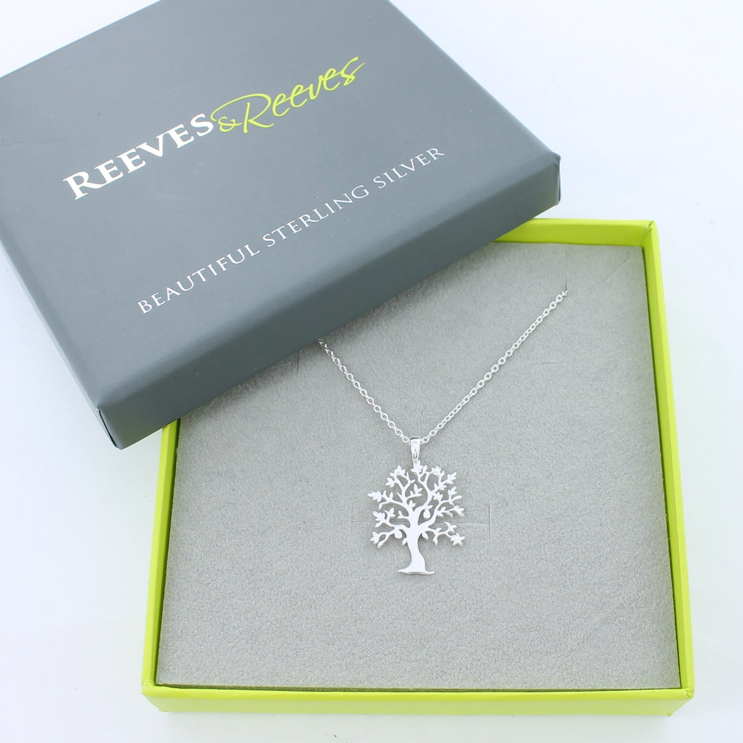 A sterling silver tree necklace with a gold plated 'nut' hanging in the branches. The pendant hangs on a silver adjustable chain and is shown in a Reeves & Reeves grey and green branded gift box.