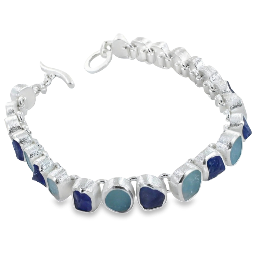 Rough cut aqua marine and tanzanite stones, set in sterling silver in a continuous design and finished with a t bar and a circular clasp.