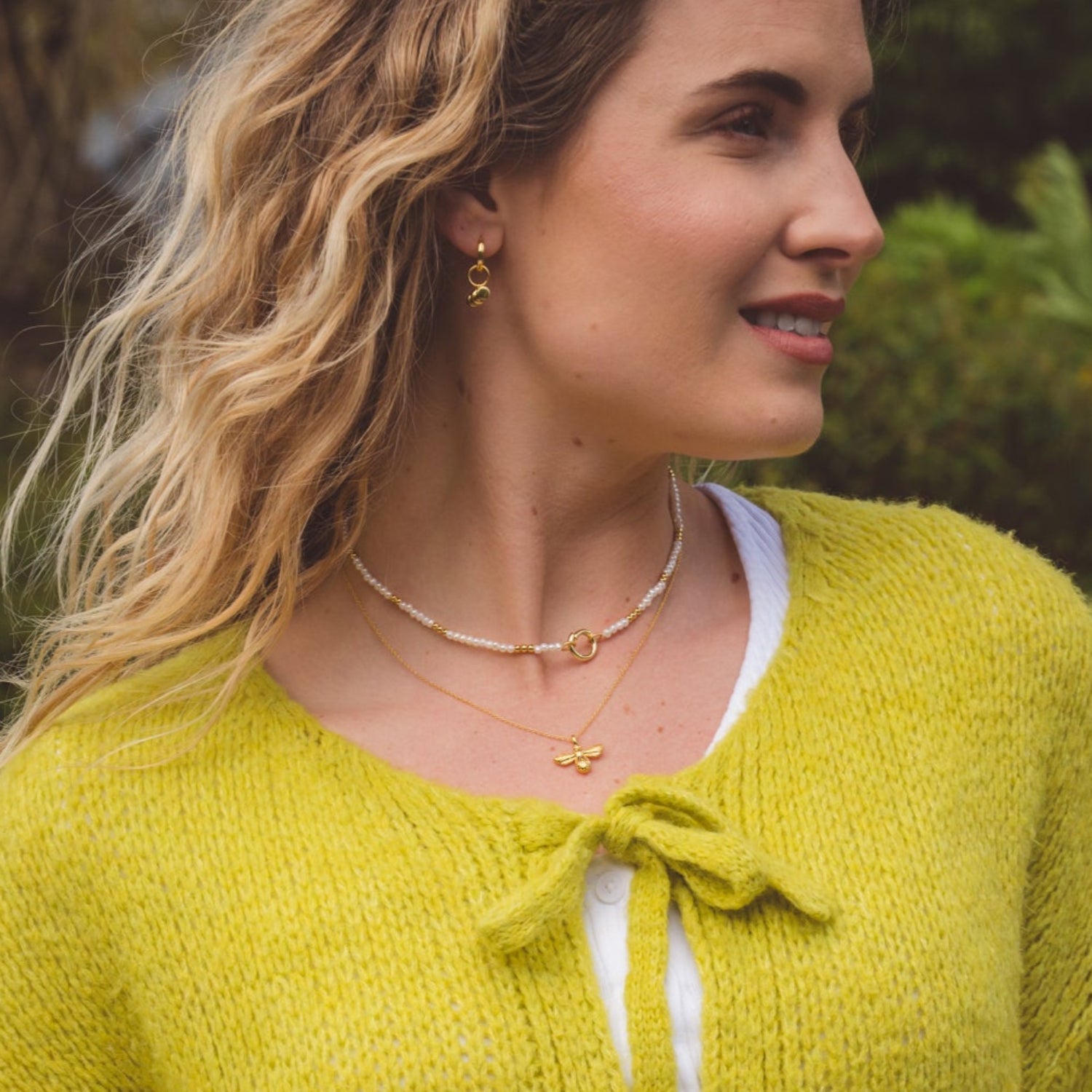 A white pearl necklace, interspersed with gold plated beads and finished with a circular clasp. Worn on a model with a gold plated bumble bee necklace.