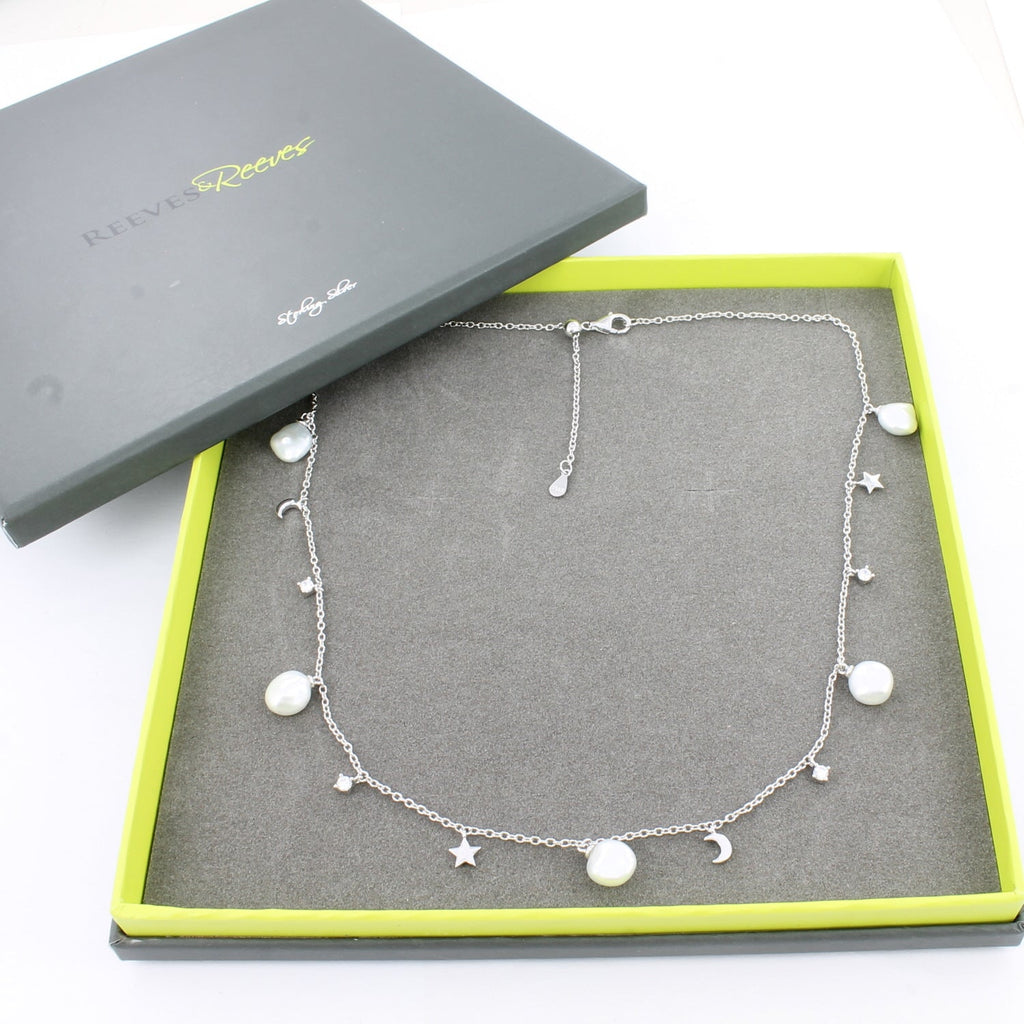 Silver necklace with white freshwater pearls, stars, moon and cubic zirconia stone charms spaced evenly around the chain. Shown in a Reeves & Reeves grey and green branded gift box.