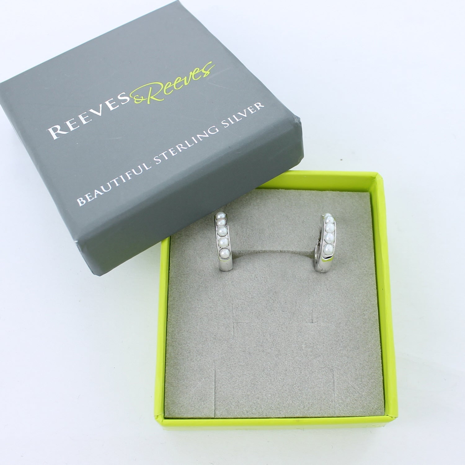Silver huggie earrings set with pearls in a Reeves & Reeves gift box.
