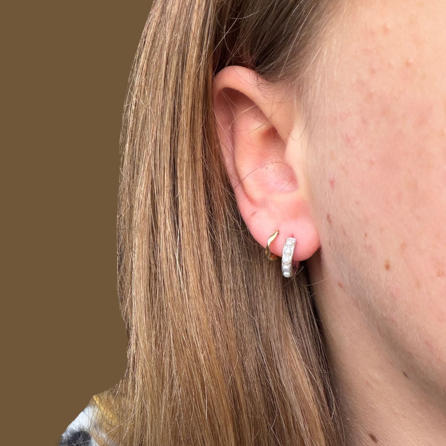 Silver huggie earring with white pearls set in the hoop, worn in a ladies ear.