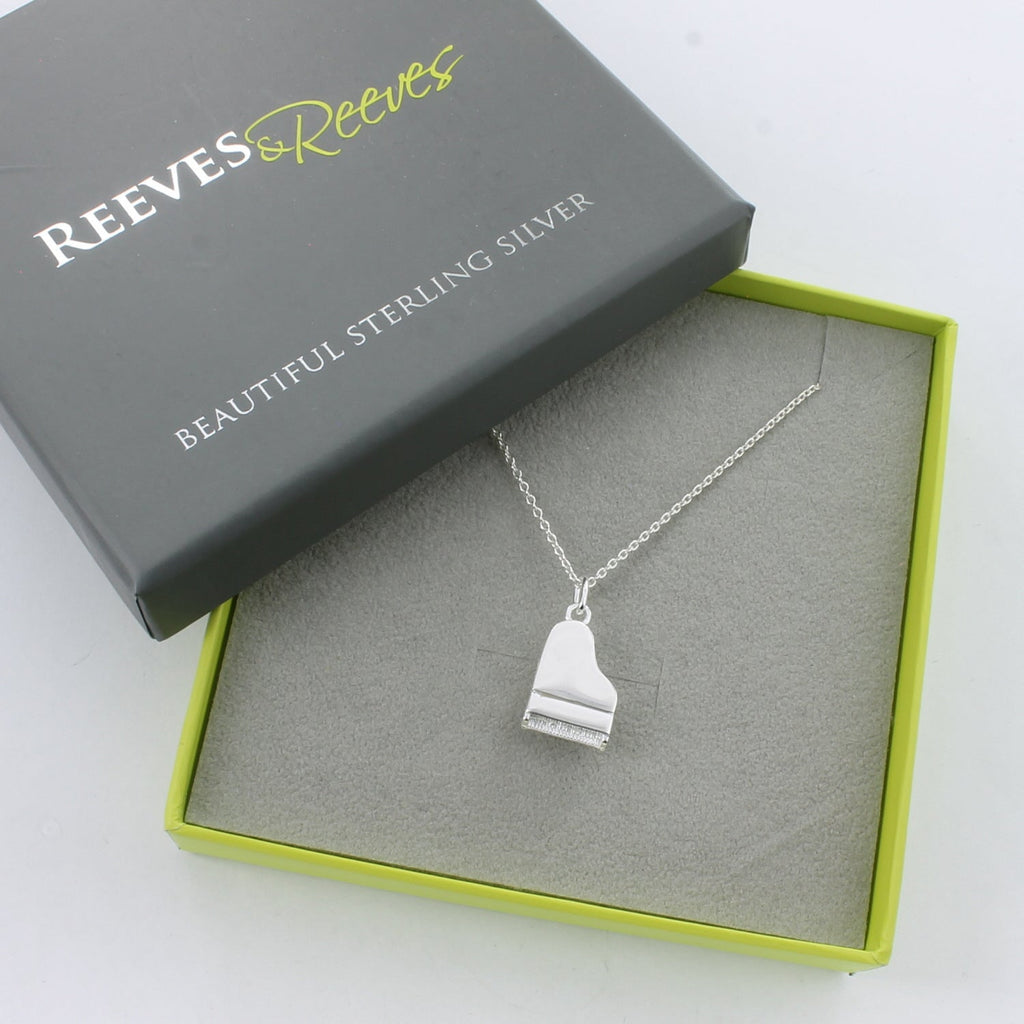 A sterling silver piano pendant, hung on a silver chain and shown in a Reeves & Reeves gift box.