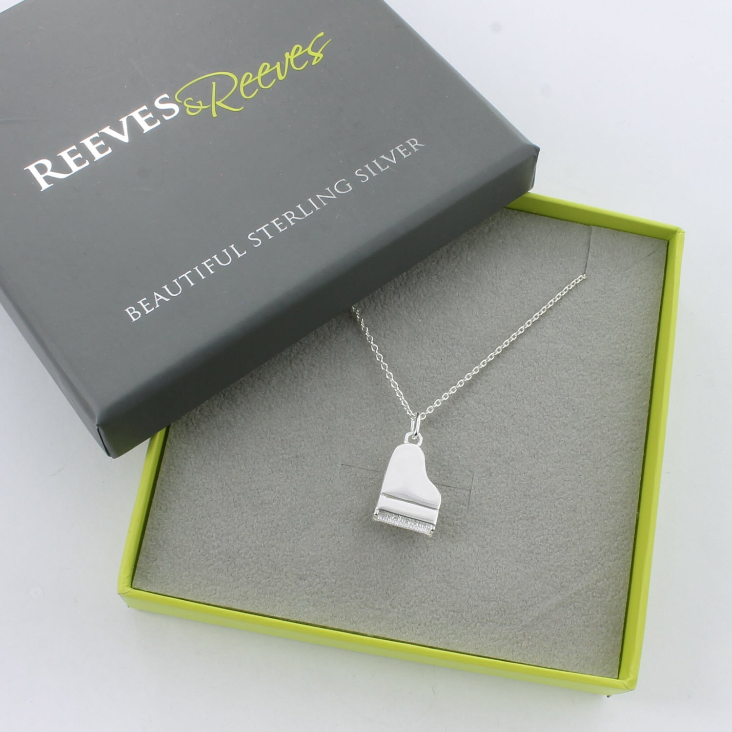 A sterling silver piano pendant, hung on a silver chain and shown in a Reeves & Reeves gift box.