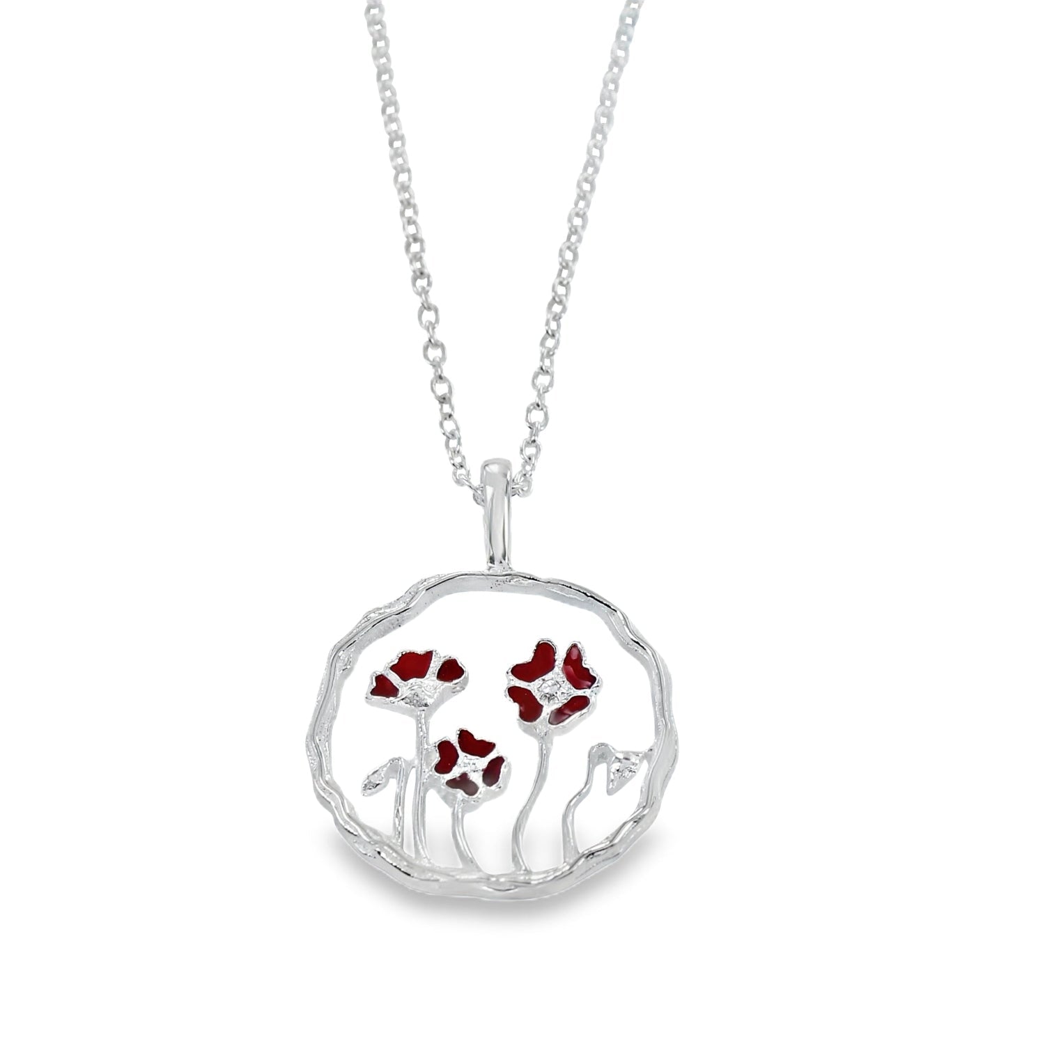 A sterling silver circular pendant with undulated edges. A poppy design sits inside the circle pendant with red enamel detail on the poppies. The design hangs on a silver adjustable chain.