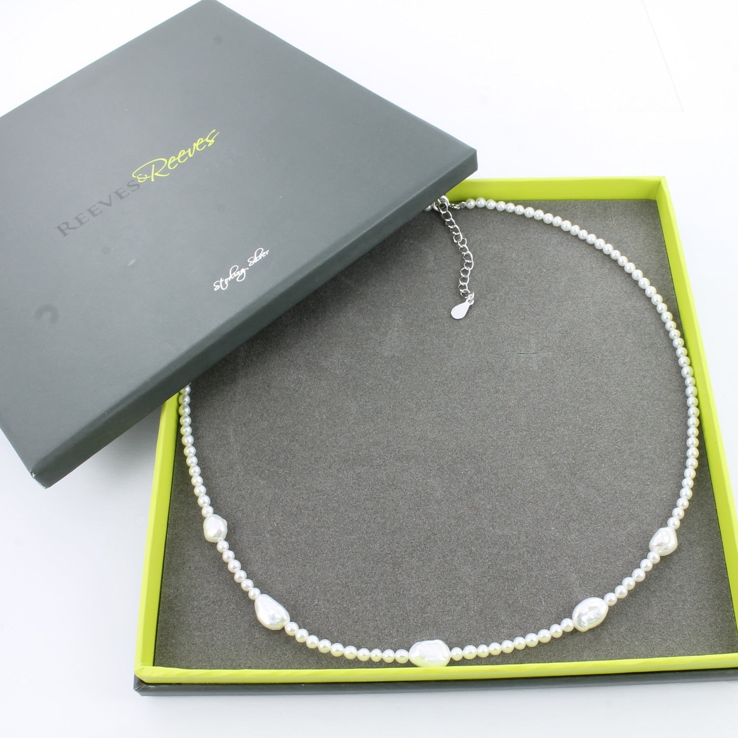 A silver and pearl necklace, with small pearls all along the chain and five larger freshwater pearls interspersed along the front of the chain. Shown in a Reeves & Reeves grey and green gift box.