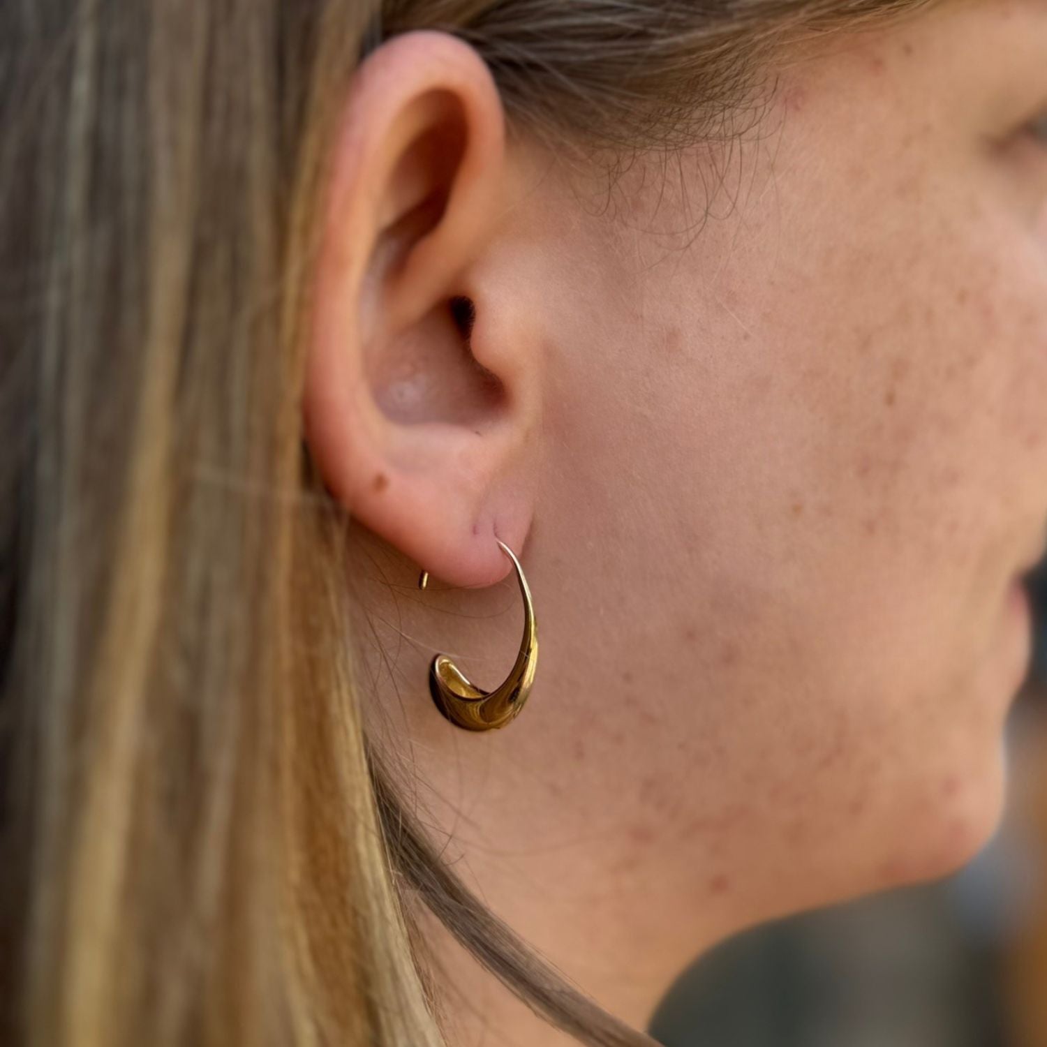 A gold plate hoop earring in a curved 'raindrop shape. Worn in a ladies ear.
