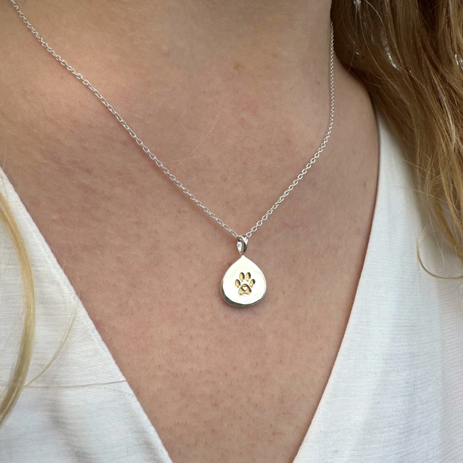 A silver teardrop shaped pendant with a gold plated pawprint design in the centre. The pendant hangs on a silver adjustable chain.
