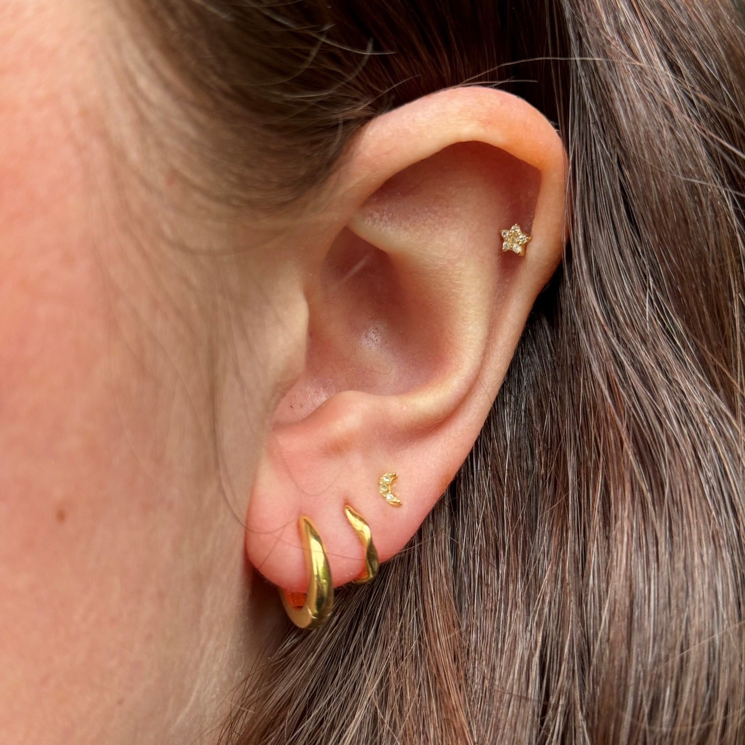 An 18ct gold plated twist huggie, shown in a ladies ear.