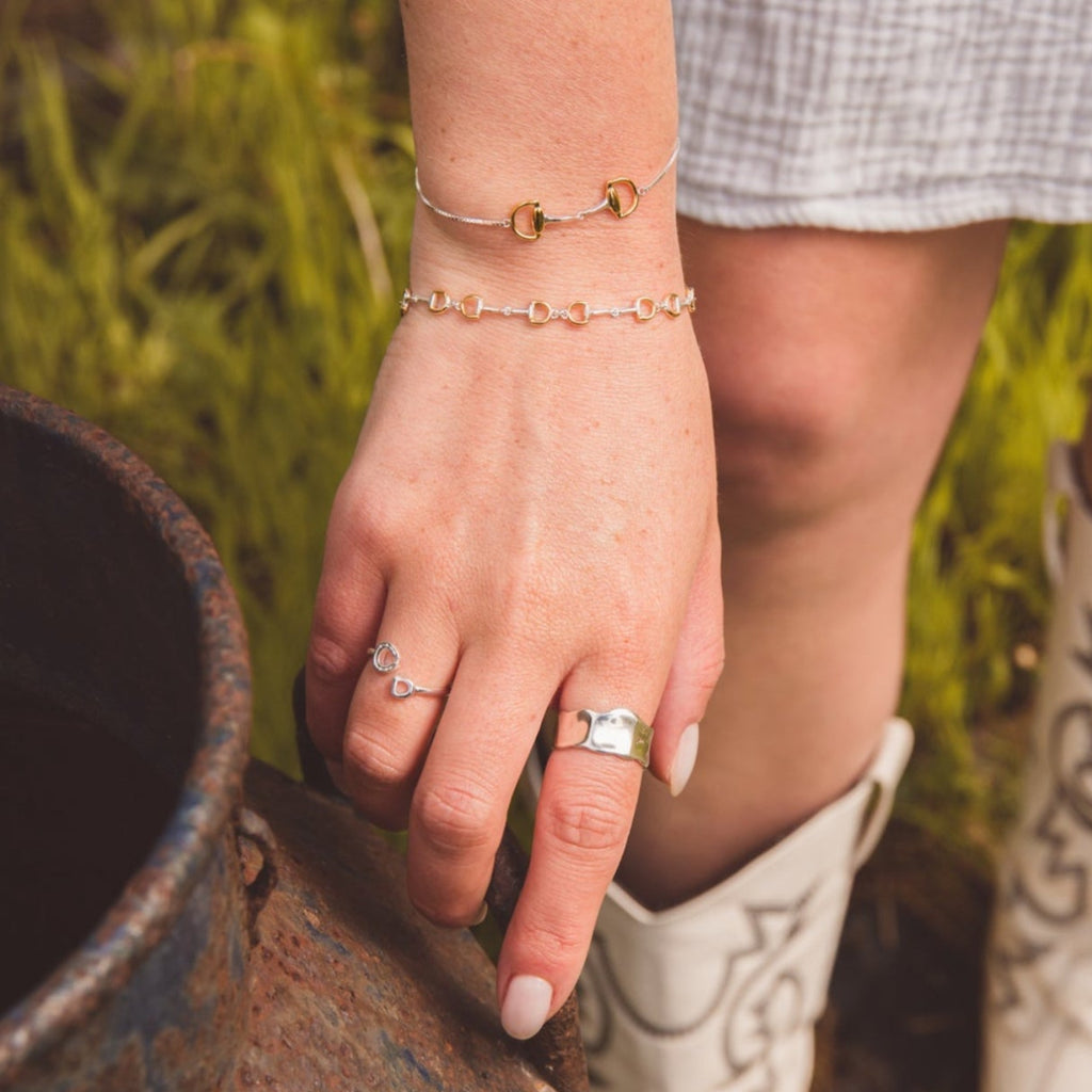 Woman wearing two snaffle bracelets in silver with gold plating.