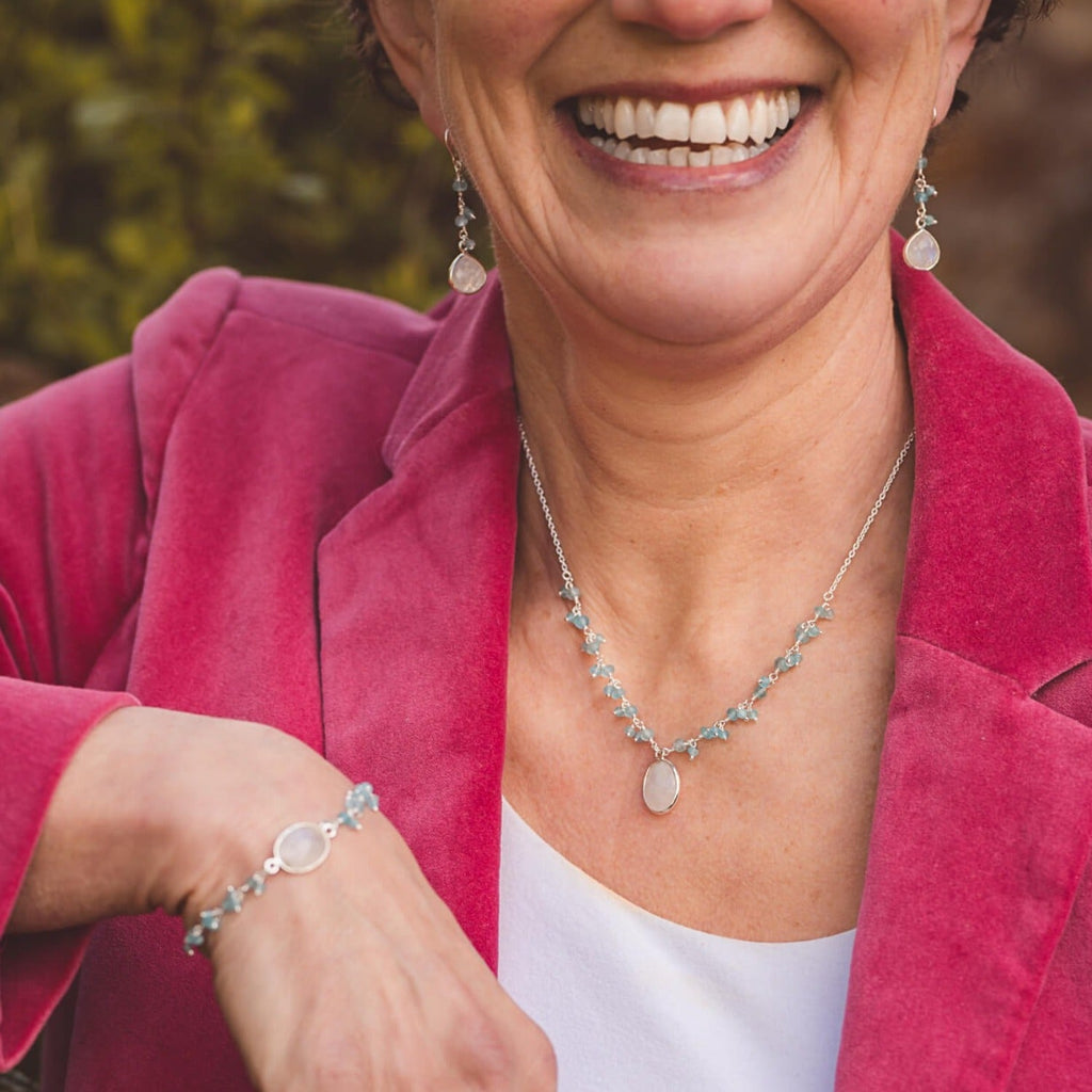 A silver chain necklace with an oval shaped moonstone hanging from the centre of the chain. Small Aqua chalcedony stones sit in clusters up either side of the chain. Model wears the necklace with the matching bracelet and drop earrings.