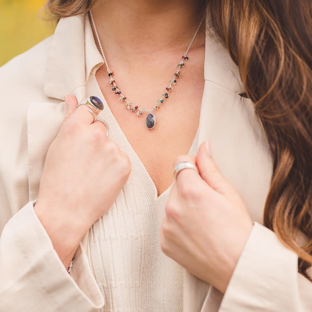 A sterling silver fine chain with oval labradorite stone set at the centre and smaller coloured stones up either side of the chain. Worn on a model.