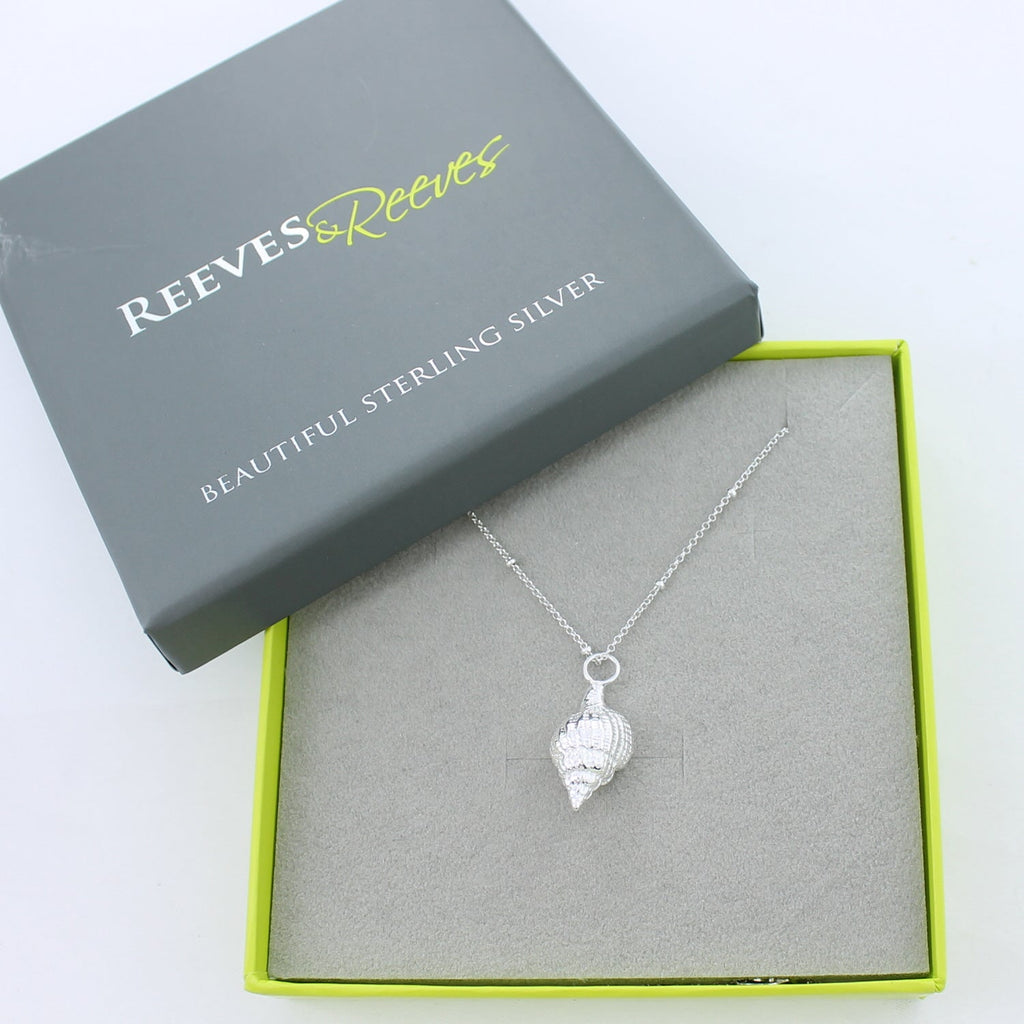 A silver Spiral Shell Necklace, hanging on a beaded fine silver chain and shown in a Reeves & Reeves branded gift box.