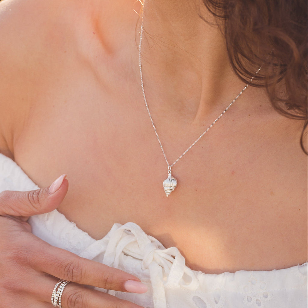A sterling silver spiral shell necklace, hung on a silver adjustable beaded chain and worn on a model.