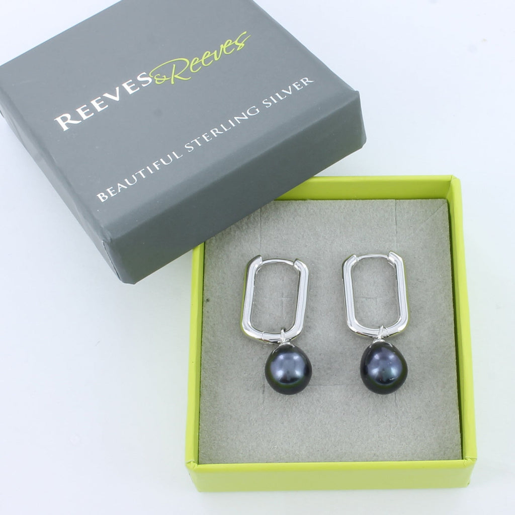 Pair of silver huggie earrings with peacock pearl charms, shown in a Reeves & Reeves grey and green branded gift box.