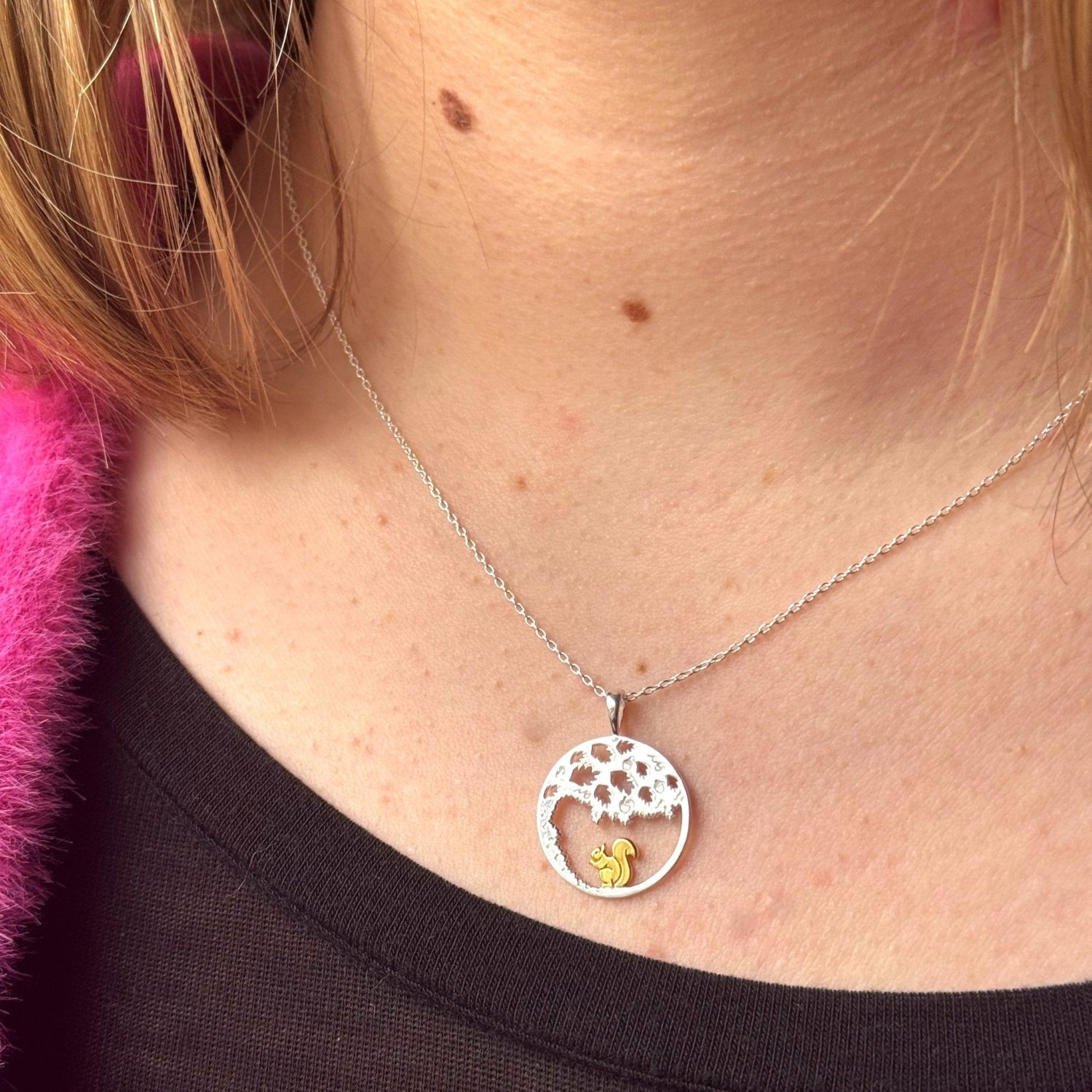 A circular pendant in sterling silver with an oak tree design and a gold plate squirrel sat inside the circle. It hangs on a silver adjustable chain and is worn on a ladies neck.