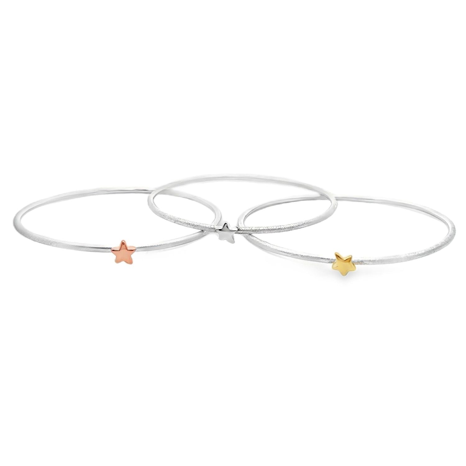 Three thin silver bangles, each with a 3D star charm at the centre, one silver, one 18ct yellow gold and one 18ct rose gold.