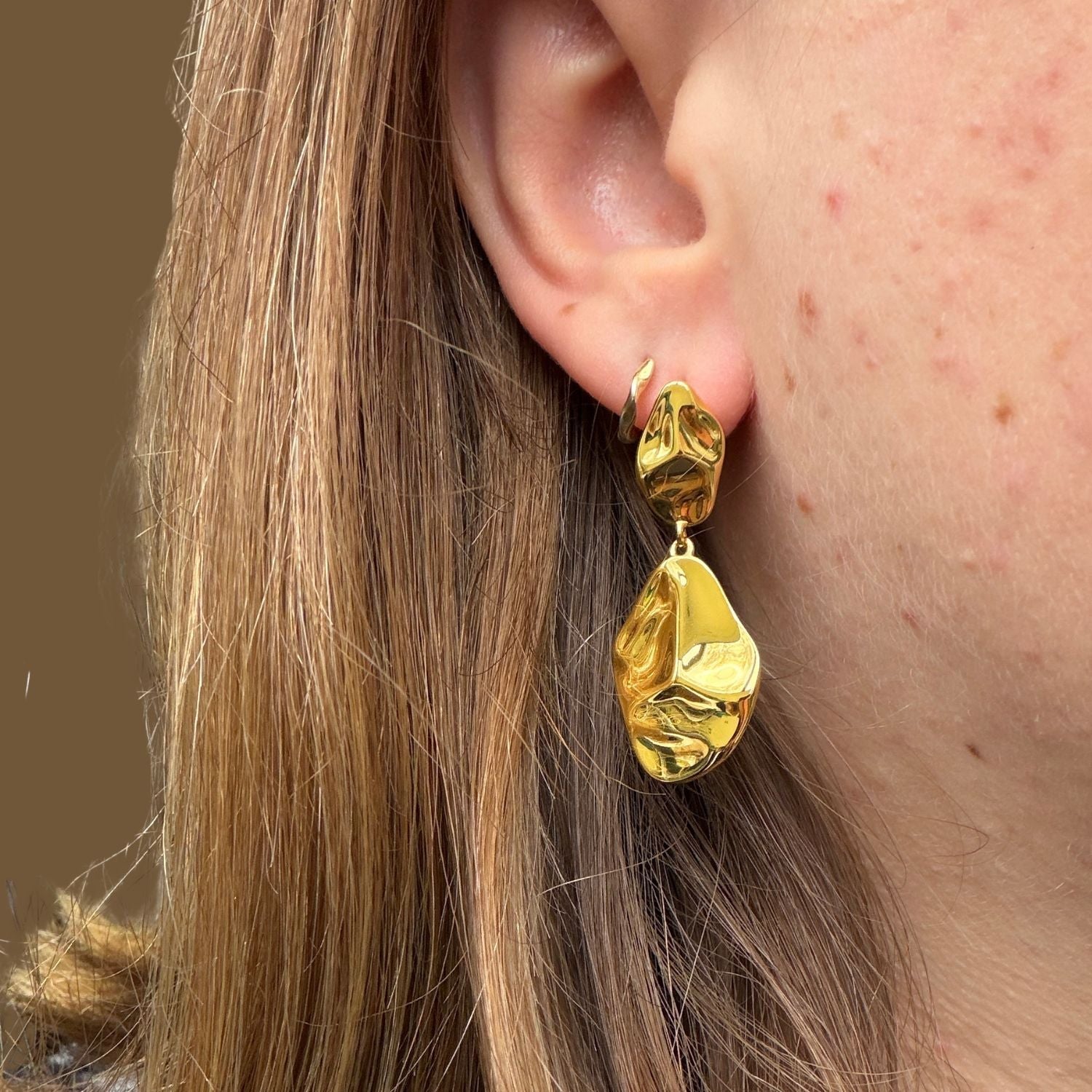 Gold plated drop earrings worn in a ladies ear.