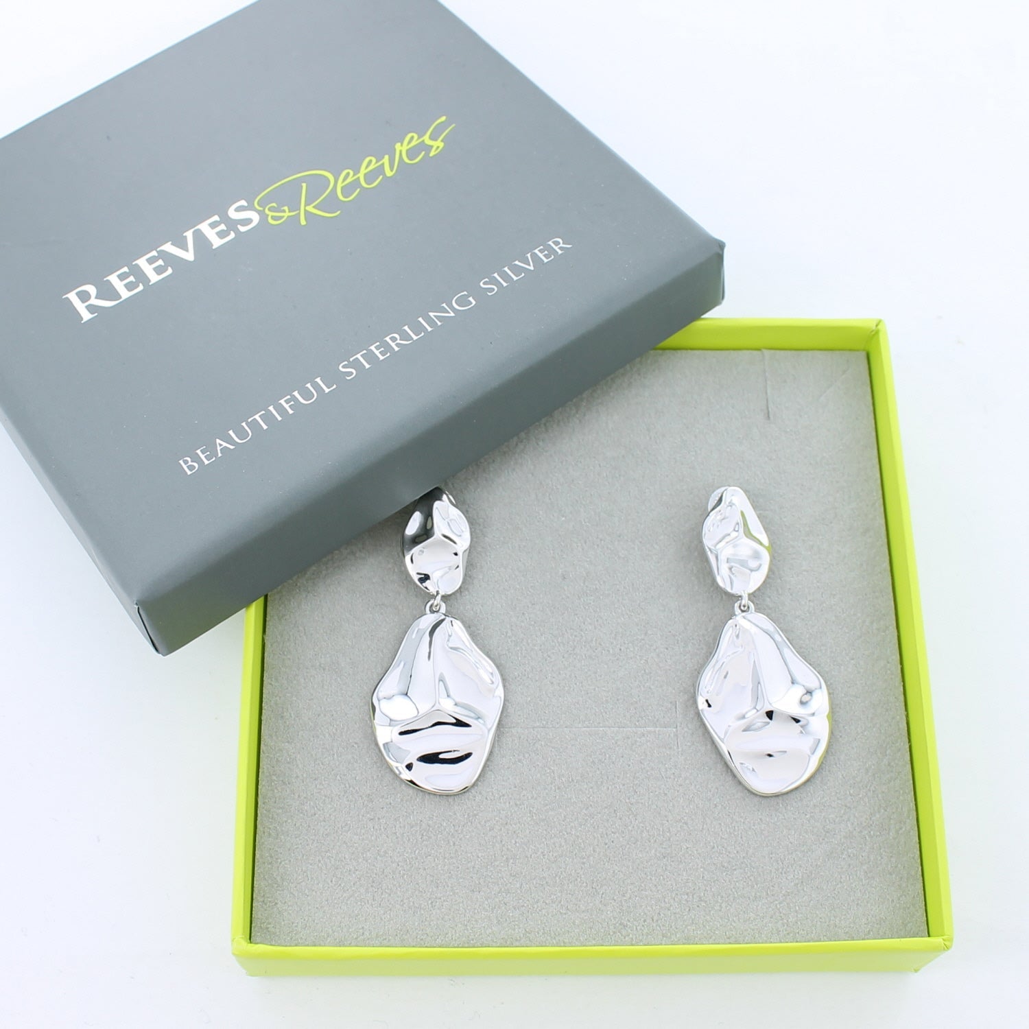 Silver drop earrings with two convex circular shapes, shown in a Reeves & Reeves grey and green branded gift box.