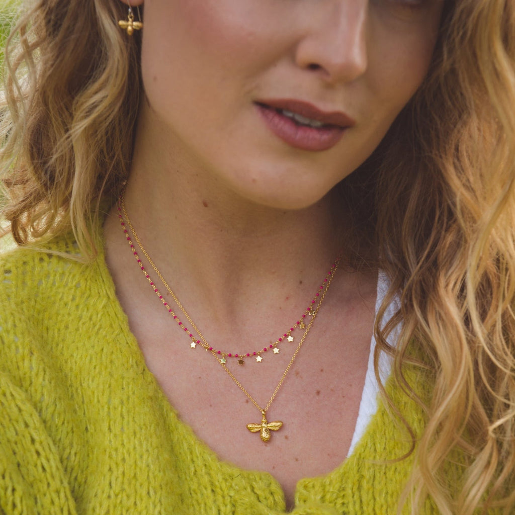Silver and gold plated pink enamel bead necklace with star charms. Layered with a gold plated bumble bee necklace and shown on a models neck.