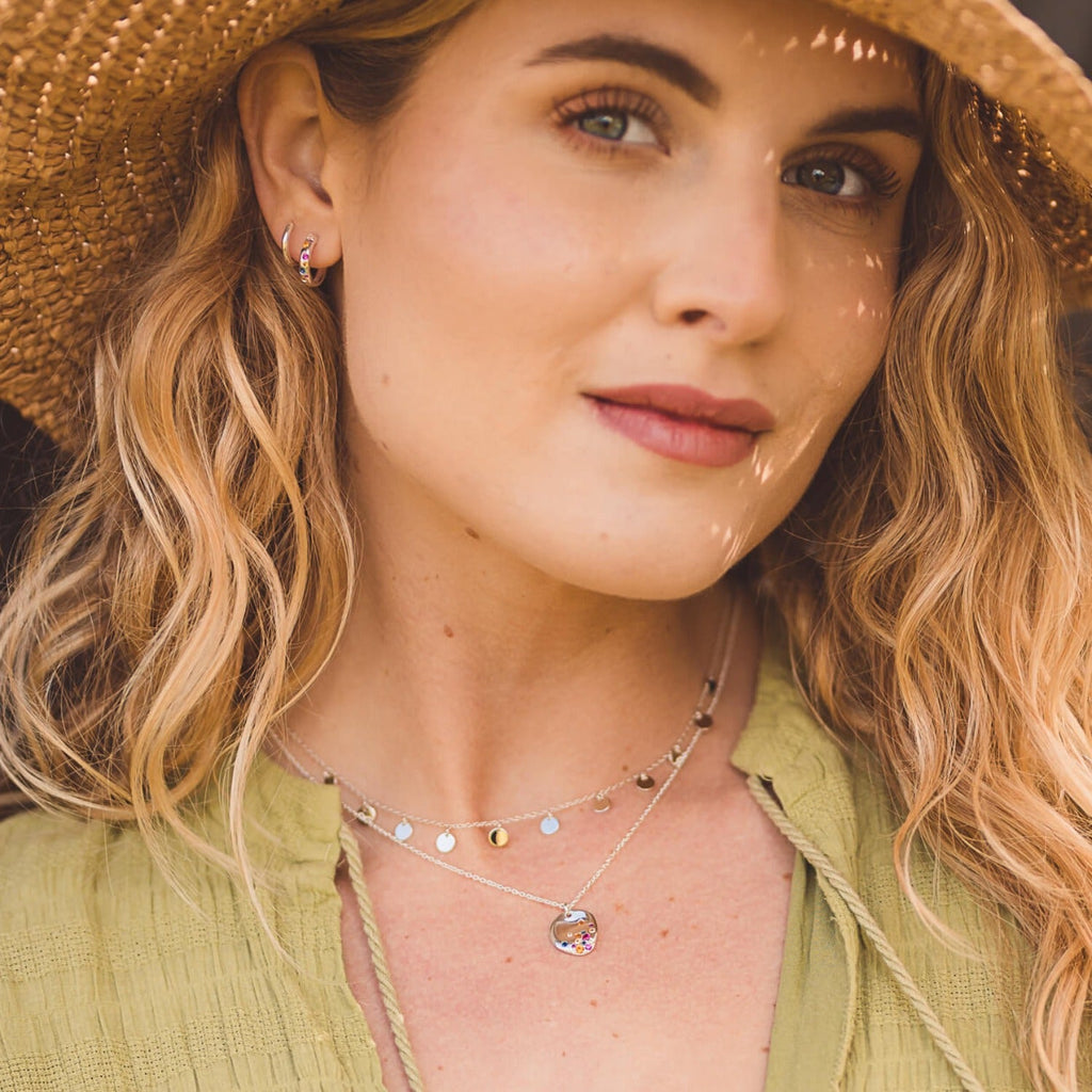 A fine silver chain with high shine flat disc charms spread evenly along the chain. The necklace is worn on a model.