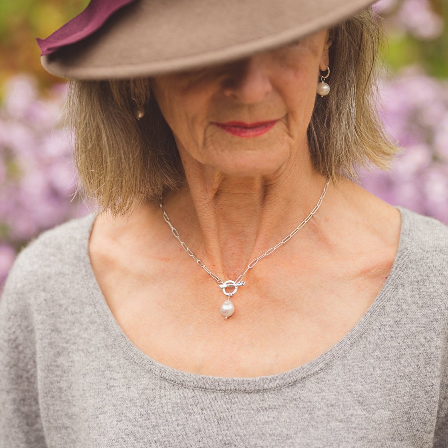 An elegant glamour pearl necklace, with a hammered disc and t bar fastening with a white freshwater pearl hanging below. The design hangs on a paperclip style chain and is worn on a model.