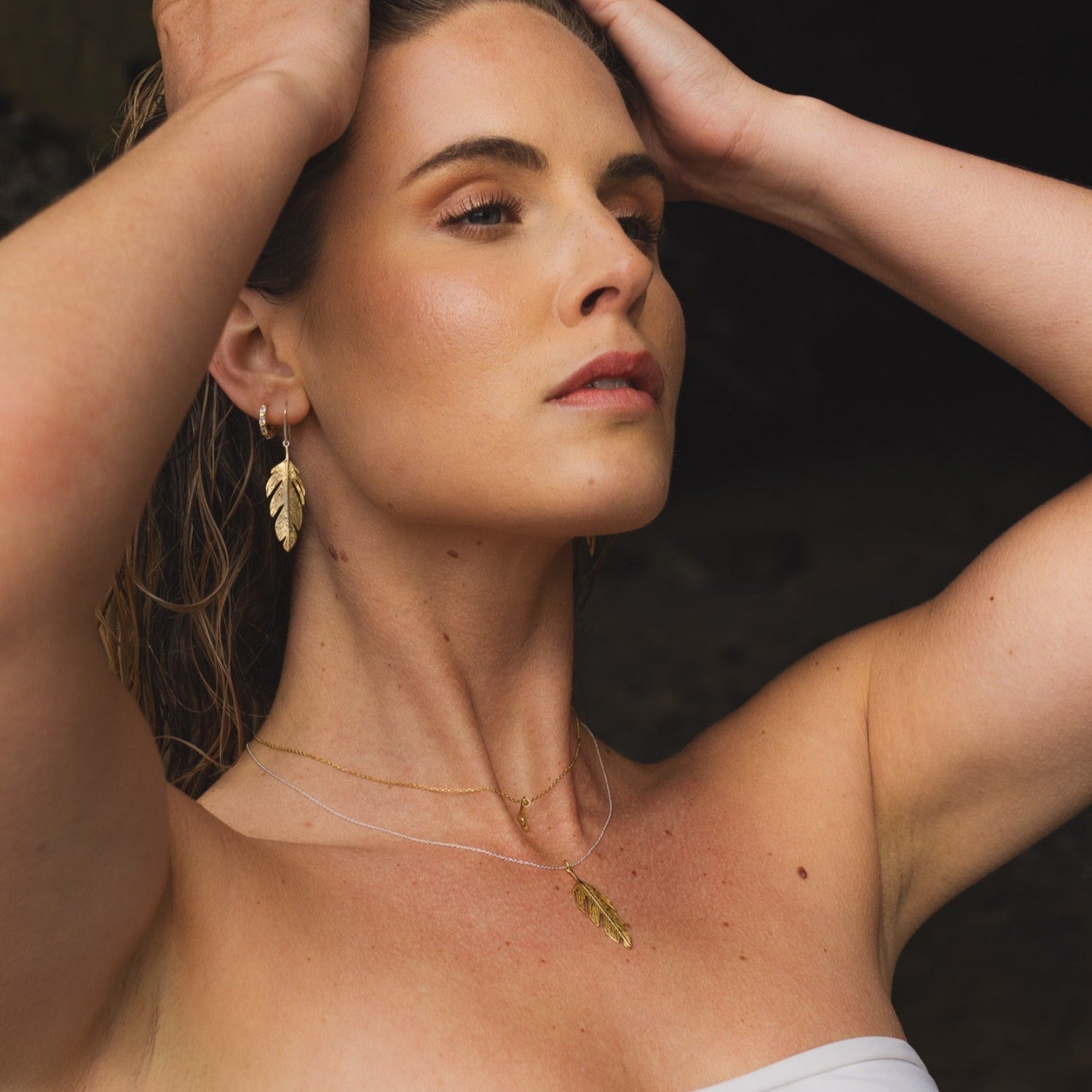 A sterling silver and 18ct gold plated large feather drop earring, on a silver hook. Shown in a ladies ear with the matching necklace.