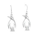 A pair of Penguin silhouette drop earrings, hanging on silver hooks.