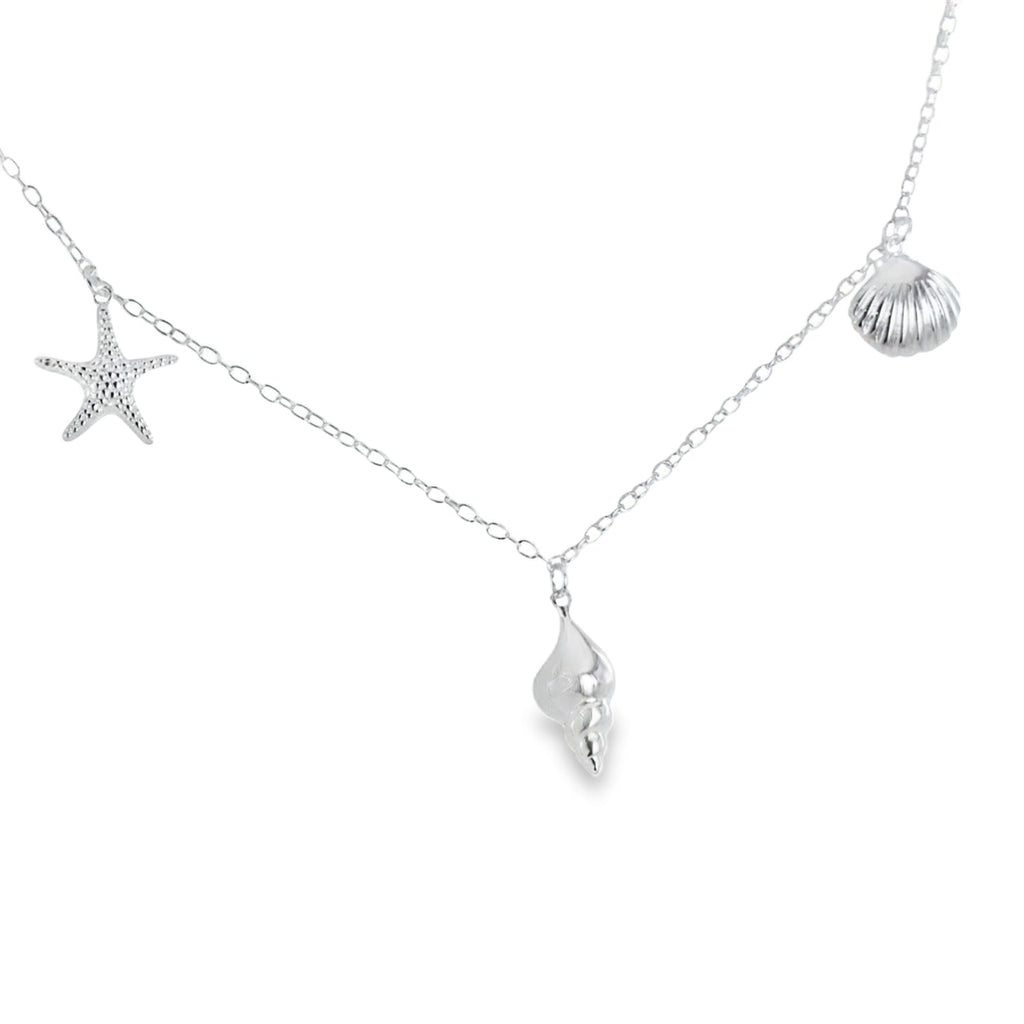 Silver chain necklace with starfish, conch shell, and scallop shell hanging as separate charms along the chain.