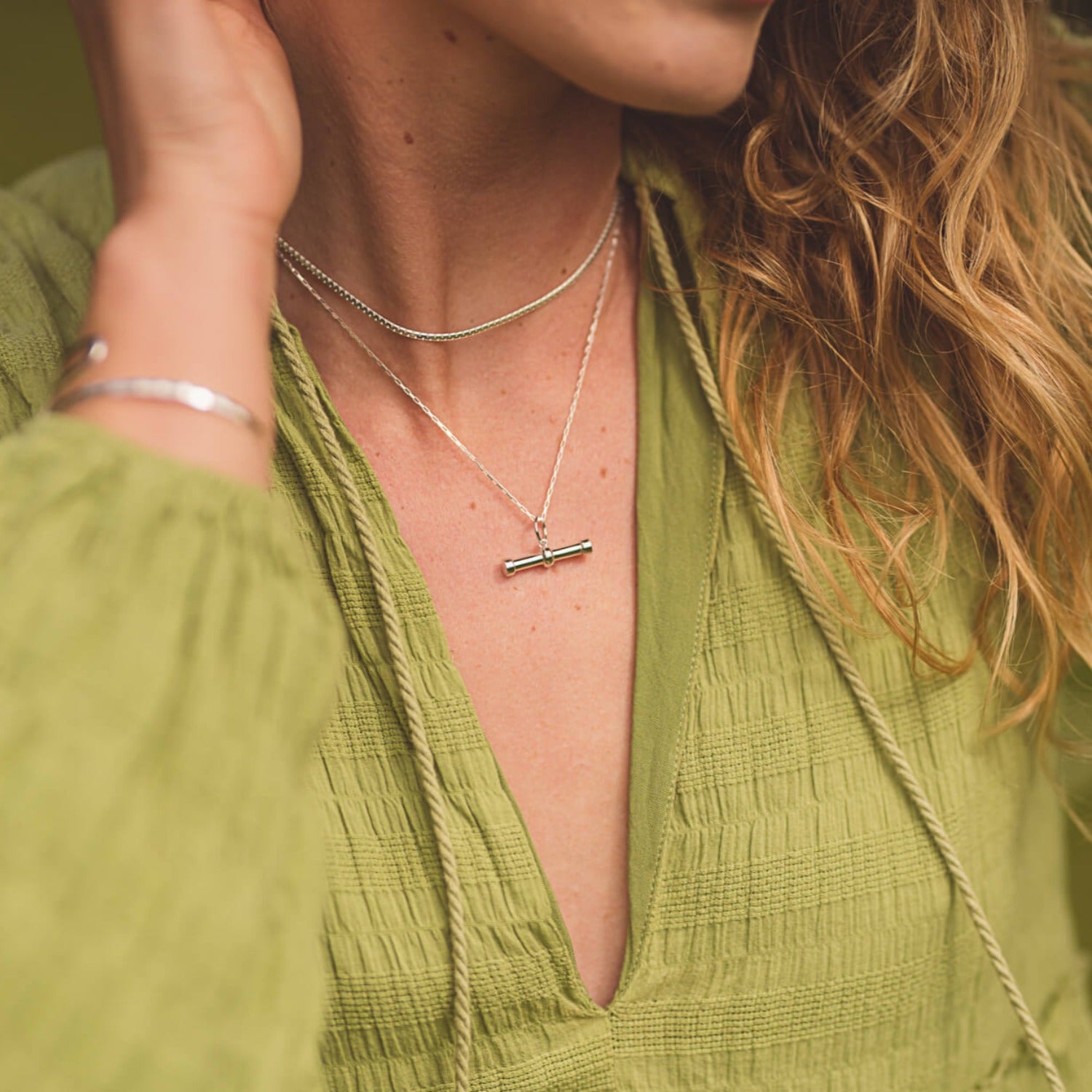 A silver T Bar necklace, hung on a silver box chain and layered with a simple snake chain. Worn on a models neck.