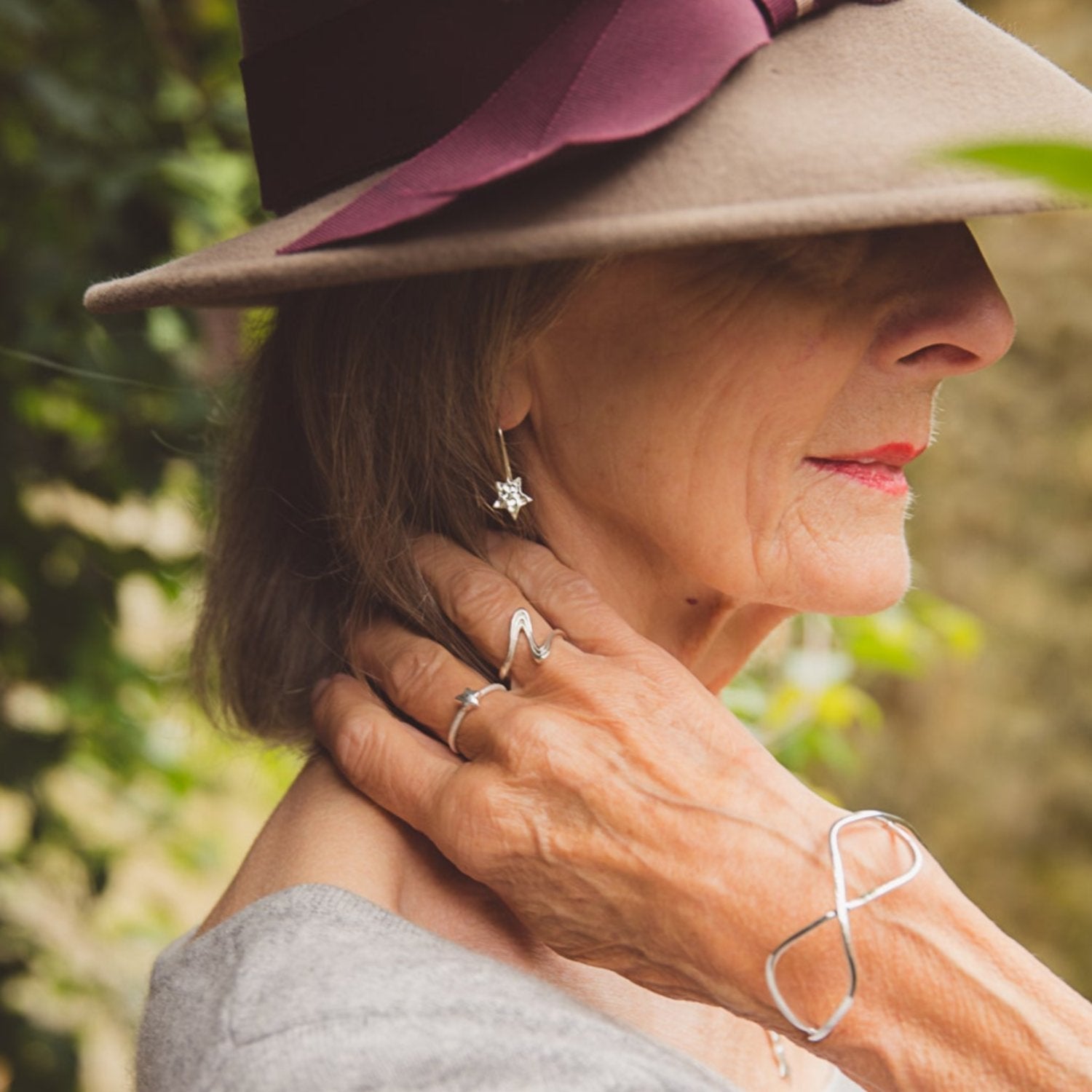 A lady wearing a pair of sterling silver drop earrings with a hammered star hanging from the bottom.