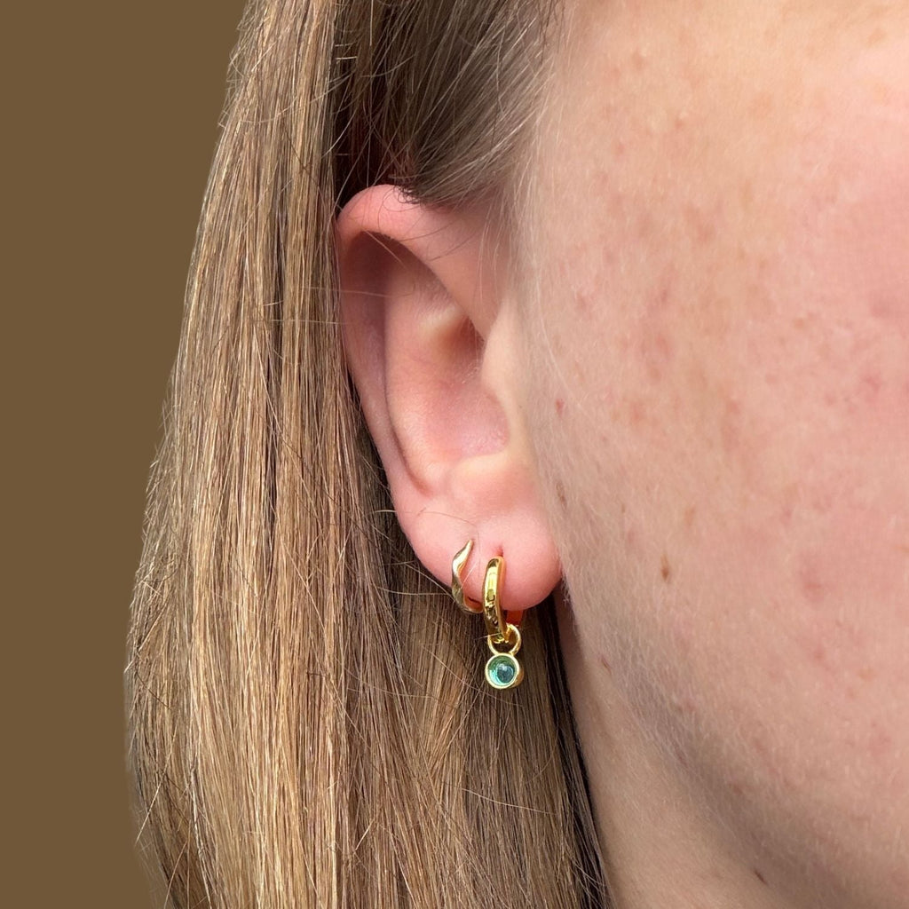 Gold plated hoop earring with a blue gemstone worn in a ladies ear.