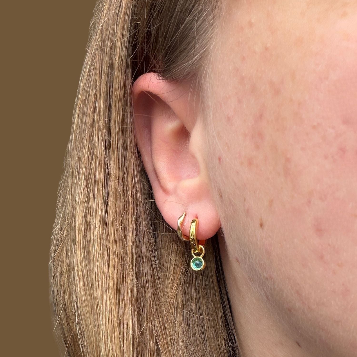 Gold plated hoop earring with a blue gemstone worn in a ladies ear.