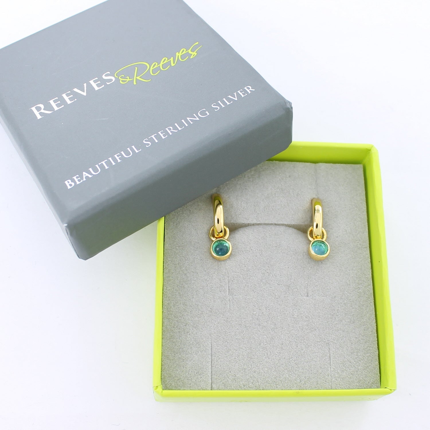 Gold plate hoop earrings with blue gemstones, shown in a Reeves & Reeves grey and green branded gift box.