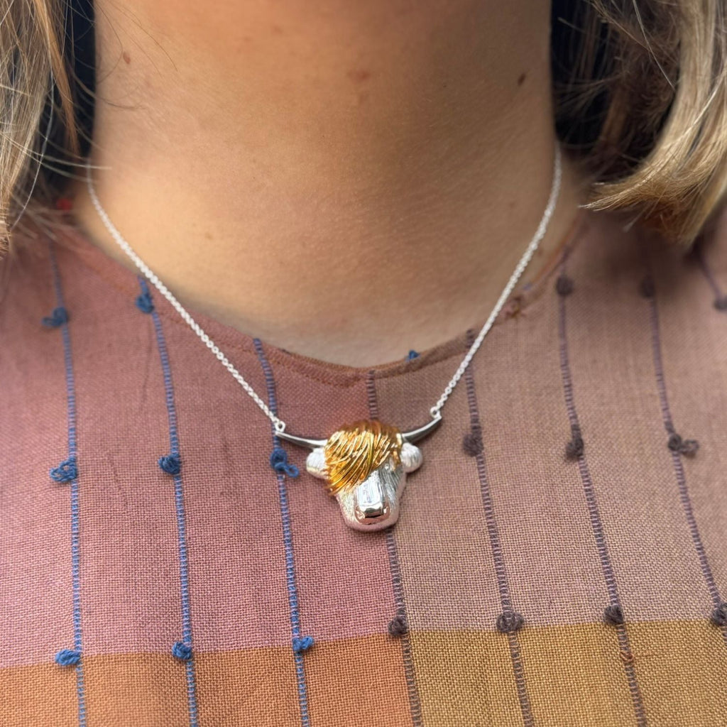 A sterling silver super size highland cow face, with 18ct rose gold plated nose, 18ct yellow gold hair and black ruthenium horns, hung centrally on a fine silver chain and worn on a model.